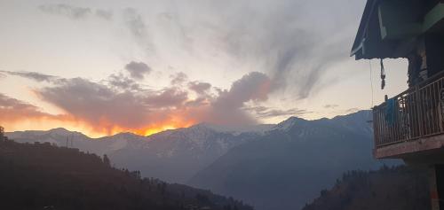 a sunset over a mountain range with the sun setting at BohOdyssey Hallan a Traditional Village Stay with Panoramic Mountain Views in Nagar