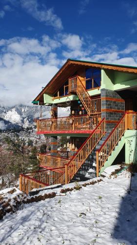 a log cabin with a deck in the snow at BohOdyssey Hallan a Traditional Village Stay with Panoramic Mountain Views in Nagar