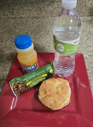 Marshall马歇尔旅行者汽车旅馆的一个红色托盘，上面放着一瓶水、一个三明治和一杯饮料。