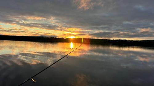 a boat in a lake with the sun setting on the water at Wild Power Guesthouse in Lycksele