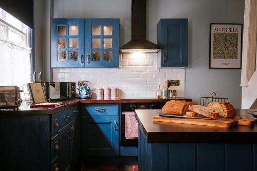 a kitchen with blue cabinets and bread on a cutting board at Bronte's Rest - Detached Elegant Cottage in Historic Old Town with Garden in Scarborough