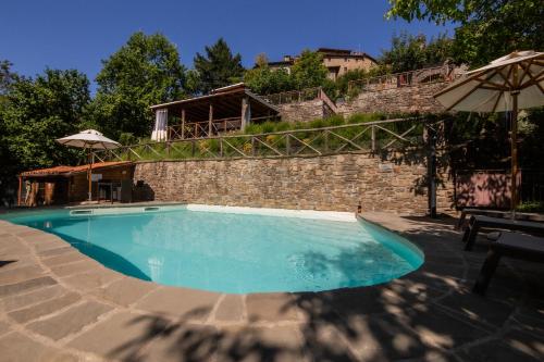 a swimming pool with a stone wall and an umbrella at Canto del Fiume in Ortignano Raggiolo