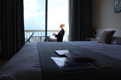 a woman standing in a hotel room with a large window at Logis Hôtel Le Calluna Restaurant La Flottille in Préfailles