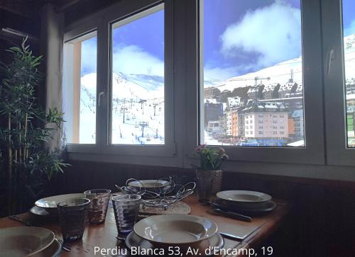 a table with plates and glasses in a room with windows at AC Apartaments Suite in Pas de la Casa