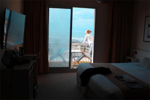 a hotel room with a woman looking out the window at Logis Hôtel Le Calluna Restaurant La Flottille in Préfailles