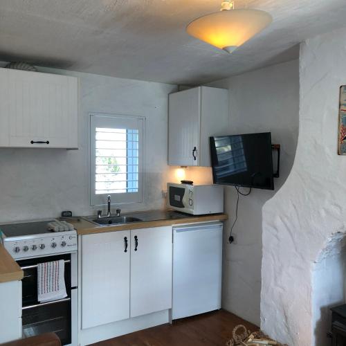 a kitchen with white cabinets and a tv on the wall at Dolphin Cottage - Child & Pet Friendly in Ballintoy