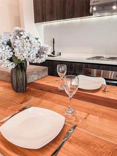 a wooden table with plates and glasses and a vase of flowers at apartamento campestre con terraza in Puerto Varas