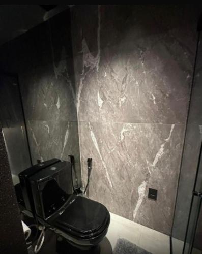 a bathroom with a black toilet and a stone wall at Get By Side - Jardim Oceania in Tambaú