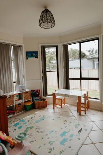 a living room with a table and chairs and windows at Sunny Dayz Shellharbour in Barrack Point