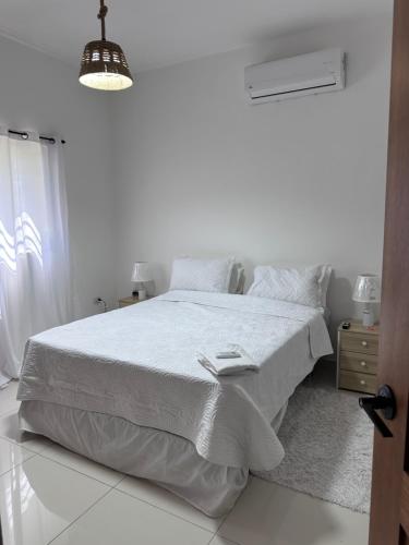 a white bedroom with a bed and a lamp at Brand New Beachfront Sunset Apartments in San Felipe de Puerto Plata