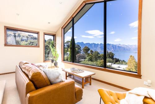 a living room with a couch and a table and large windows at Spectacular LAKE View in Queenstown