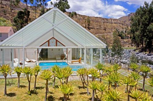 a glass house with a pool in a field with trees at Aranwa Pueblito Encantado del Colca in Coporaque