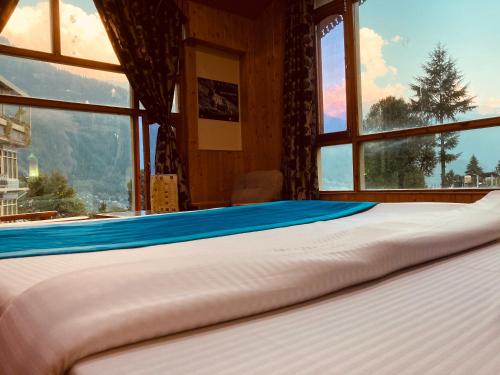 a bed in a room with a large window at Woods Villa Cottages Manali - 1,2,3,4 Cottages & Villas Available in manali with scenic mountain view in Manāli