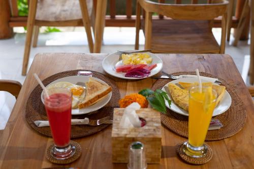 - une table en bois avec deux assiettes de nourriture et deux boissons dans l'établissement Nusa Dewata Cottage, à Nusa Penida