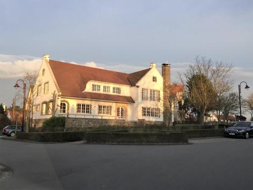 een groot wit huis met een bruin dak bij Villa D'este in De Haan
