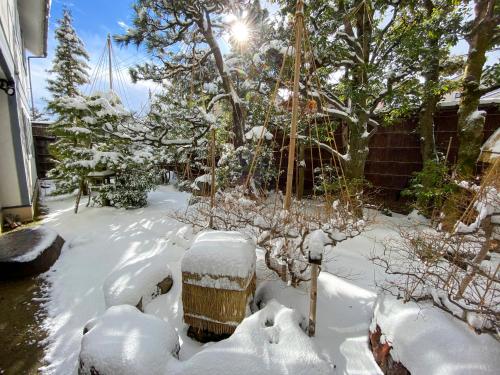 a yard covered in snow with trees and a house at Camellia Inn Yukitsubaki in Kanazawa