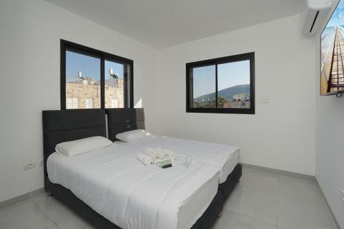 a bedroom with a large white bed with two windows at לוי-קיישן מגוון דירות גן ופנטהאוזים וסוויטות נוף ברחוב הצנחנים in Tiberias