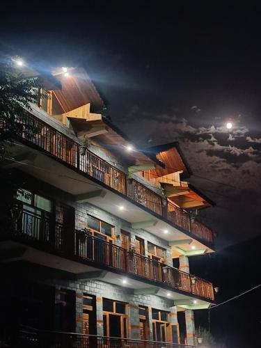a building with balconies at night with the moon at BohOdyssey Hallan a Traditional Village Stay with Panoramic Mountain Views in Nagar