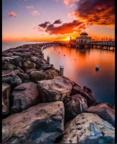 a sunset over a pier with a lighthouse in the water at Luxury Mansion Loft by the Beach in Melbourne
