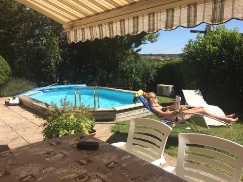 une femme assise dans une chaise à côté d'une piscine dans l'établissement Une ou deux Chambres Spacieuses, à Combles-en-Barrois