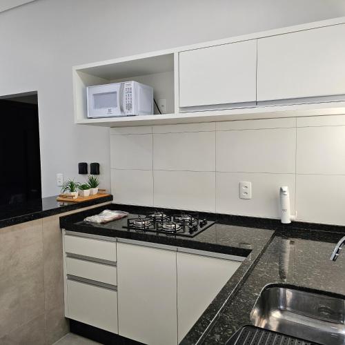 a white kitchen with a stove and a microwave at Louvre Residence 202, conforto, estacionamento e wi-fi in Sinop