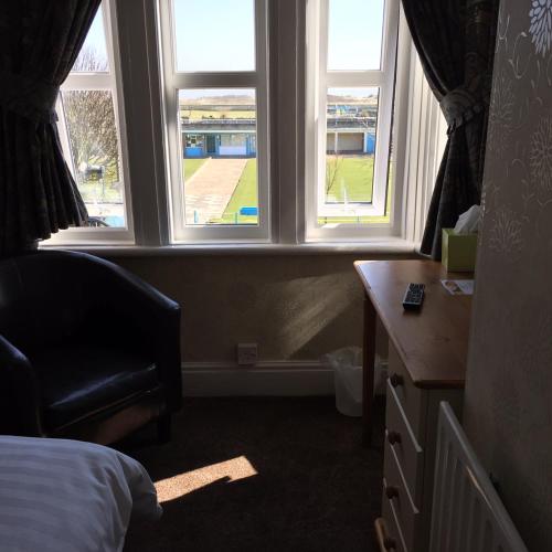 a bedroom with two windows and a desk and a chair at Woodthorpe Hotel in Skegness