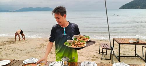 a man holding a plate of food on the beach at Yuyu Golden Beach in Ko Chang