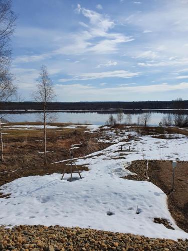 a field with snow on the ground next to a lake at Uiton kotirantasauna in Kiemunkivaara