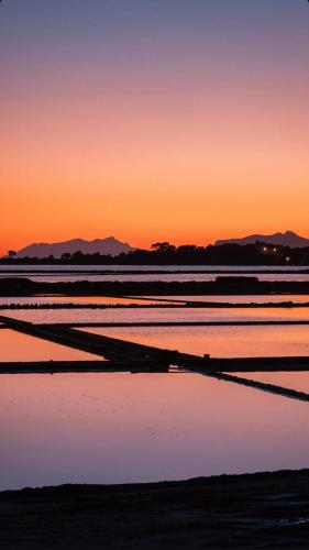 a sunset over the water with mountains in the background at Oikos Rooms in Marsala