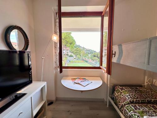a room with a window and a table and a tv at OSPEDALETTI Mare e Relax- Affittasi "Oasi Riviera" con campo da Tennis e Sala Giochi in Ospedaletti