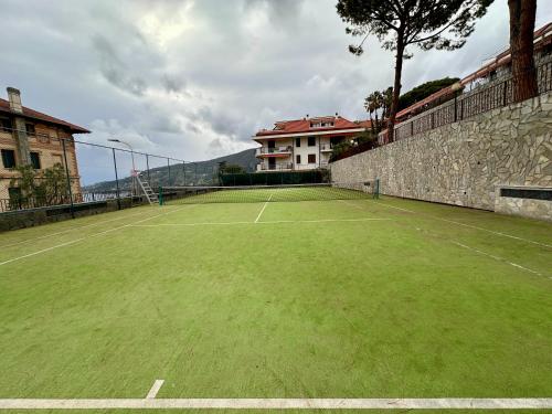 a tennis court with green grass and a building at OSPEDALETTI Mare e Relax- Affittasi "Oasi Riviera" con campo da Tennis e Sala Giochi in Ospedaletti