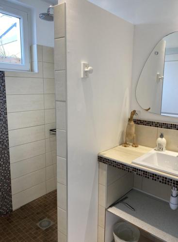 une salle de bain blanche avec un lavabo et un miroir dans l'établissement La Petite Maison, à Port-en-Bessin-Huppain