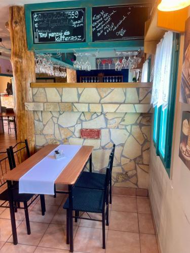 a table and chairs in a restaurant with a stone wall at Turul Panzió&Pizzéria in Szólád