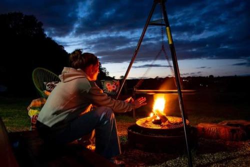a woman sitting in front of a fire at Hertford belltent farm stay riverside firepit bbq in Hertford