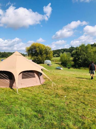 a man walking past a tent in a field at Hertford belltent farm stay riverside firepit bbq in Hertford