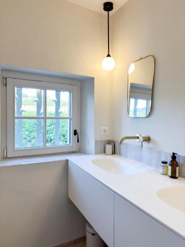 une salle de bain blanche avec deux lavabos et une fenêtre dans l'établissement Mas des Collines, à Saint-Hippolyte-le-Graveyron