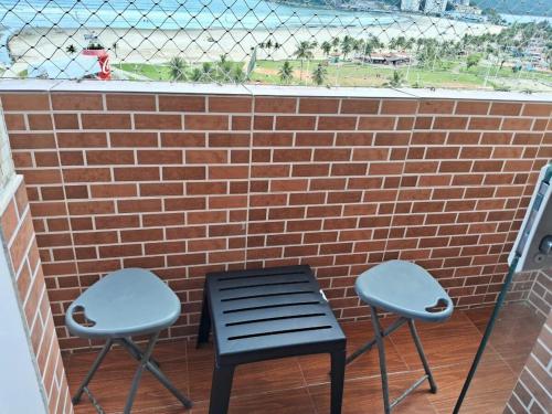 two chairs and a bench on a balcony with a brick wall at Studio São Lucas super localizado frente praia in São Vicente