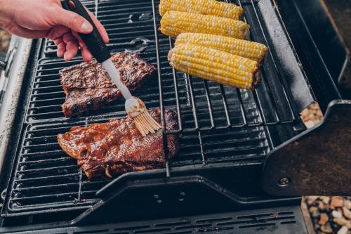 a person cooking steak and corn on a grill at Candlewood Suites Harrisonburg by IHG in Harrisonburg
