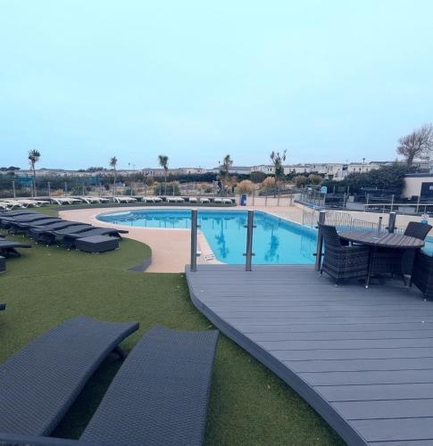 a large swimming pool with benches and a wooden deck at BEAUTIFUL LUXURY Caravan HAVEN LITTLESEA STUNNING VIEWS Sleeps 6 in Weymouth