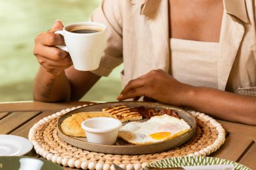 a person holding a cup of coffee and a plate of breakfast food at Zirwa Hotel Boutique - Dentro del Parque Tayrona in El Zaino