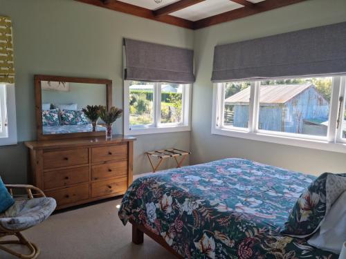 a bedroom with a bed and a dresser and two windows at Waitawheta Cottage in Waihi
