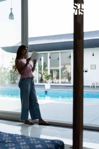 a woman reading a book in front of a pool at StayVista's Kundan Villa - Pet-Friendly Villa with Sprawling Lawn, Outdoor Pool in Jaipur