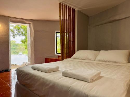 a bedroom with a large white bed with a window at บ้านดิน 2 ชั้น in Khanong Phra