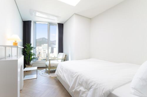 a white bedroom with a bed and a window at Brown Suites Busan Station in Busan