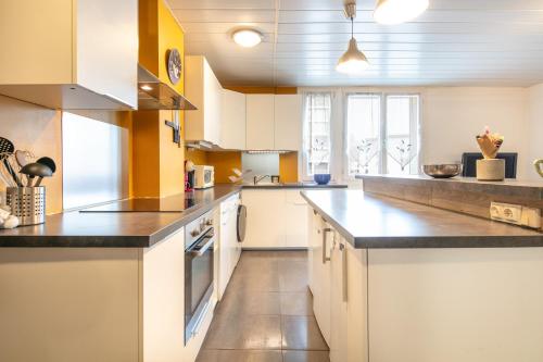 une grande cuisine avec des armoires blanches et des comptoirs noirs dans l'établissement Le Nova - 15min de Grenoble parking, à Saint-Martin-dʼHères