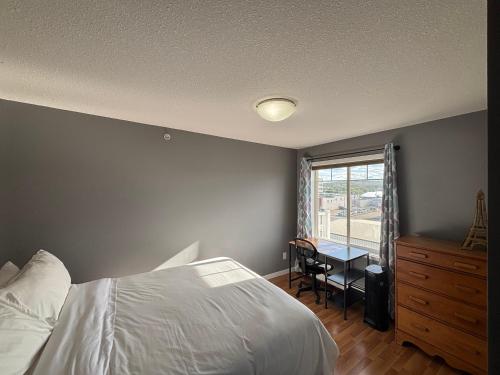 a bedroom with a bed and a desk and a window at Top Floor Riverfront Condo with Stellar Sunsets! in Fort McMurray