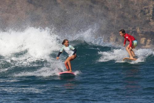 two children riding a wave on surfboards in the ocean at ekasboardriders surf&stay in Ekas