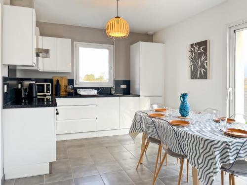 une cuisine blanche avec une table, des chaises et un chiffon de table dans l'établissement Villa Ti Ar Mor - Jardin & Plages à 300m, à Hirel