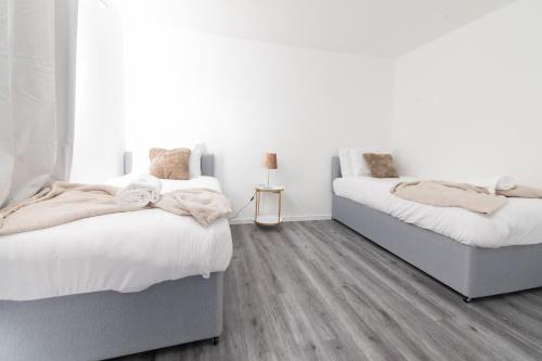 2 letti in una camera da letto con pareti bianche e pavimenti in legno di Renfrew House a Renfrew