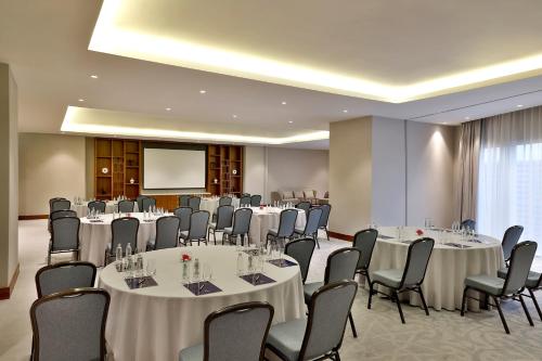 a conference room with tables and chairs and a screen at Hilton Al Khobar King Fahd Causeway in Al Khobar